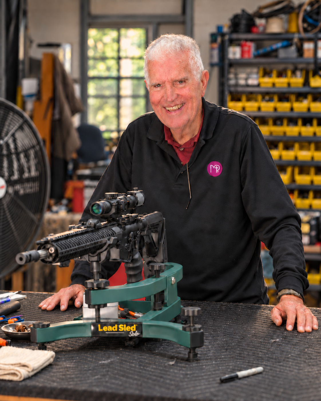 Dick Jones smiling beside a rifle in his workshop